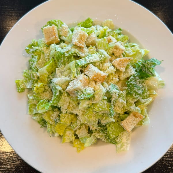 A white plate filled with Caesar salad, featuring crisp romaine lettuce, croutons, and grated Parmesan cheese.