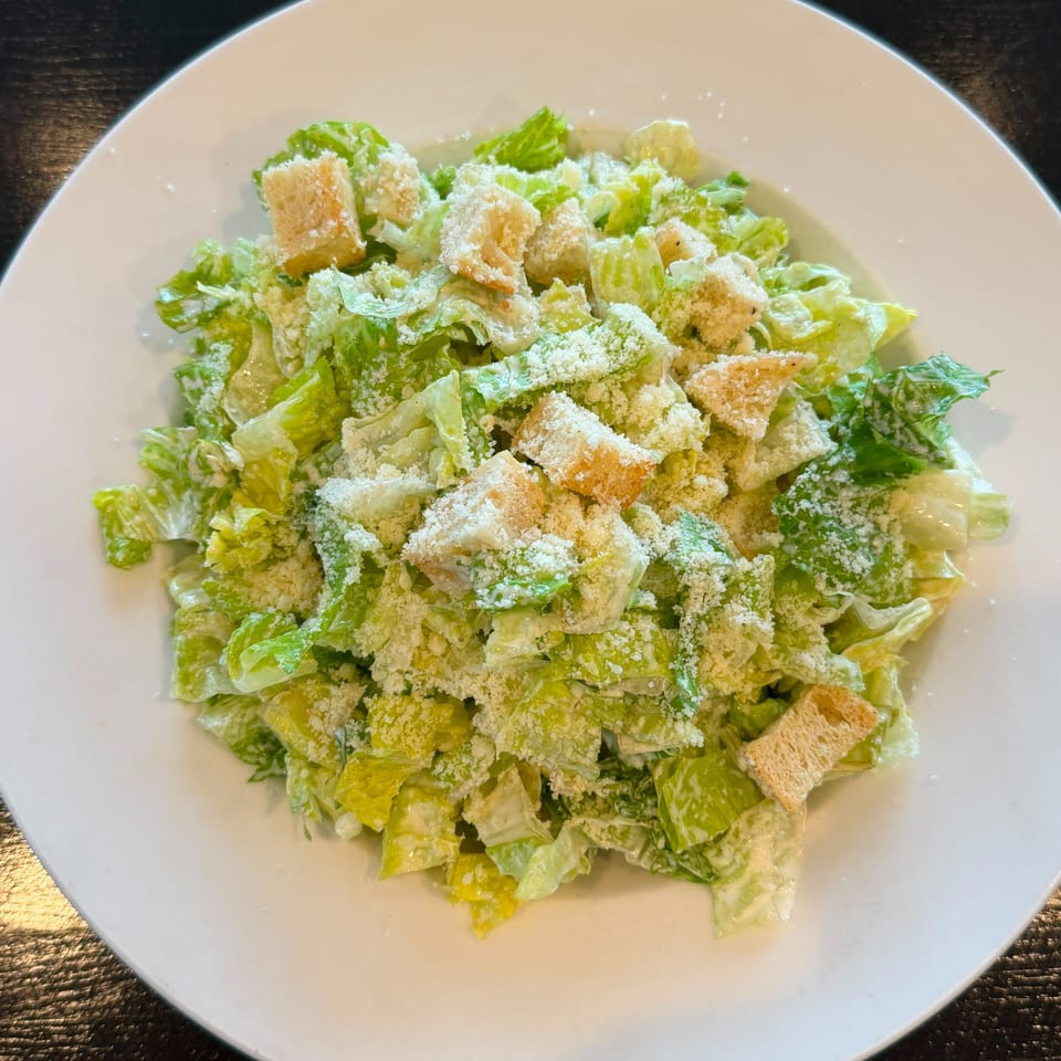 A white plate filled with Caesar salad, featuring crisp romaine lettuce, croutons, and grated Parmesan cheese.