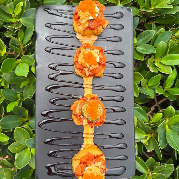 Four fried sushi rolls with orange roe and sauce, drizzled with dark glaze on a black plate.