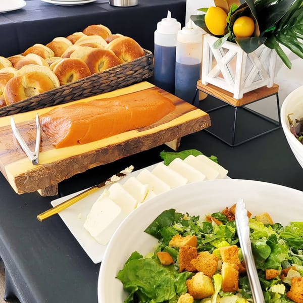 A buffet spread with bagels, salmon, cheese, and Caesar salad on a black tablecloth.