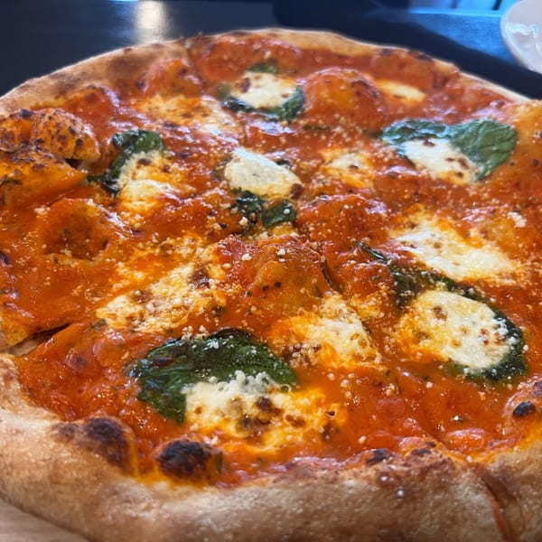 Close-up of a Margherita pizza with bright red sauce, fresh mozzarella, basil, and a crispy crust.