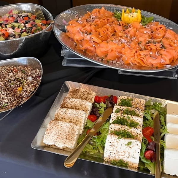 A buffet spread with smoked salmon, feta cheese, and two salads in silver bowls.