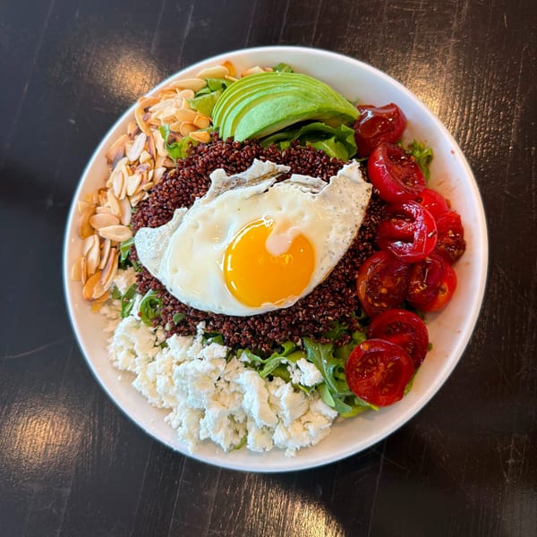 A colorful quinoa bowl with a fried egg, avocado, tomatoes, feta, and almonds.